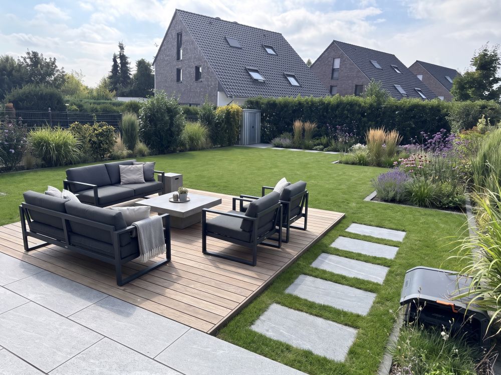 Derselbe Garten mit Holzterrasse, Lounge-Möbeln und angelegten Beeten